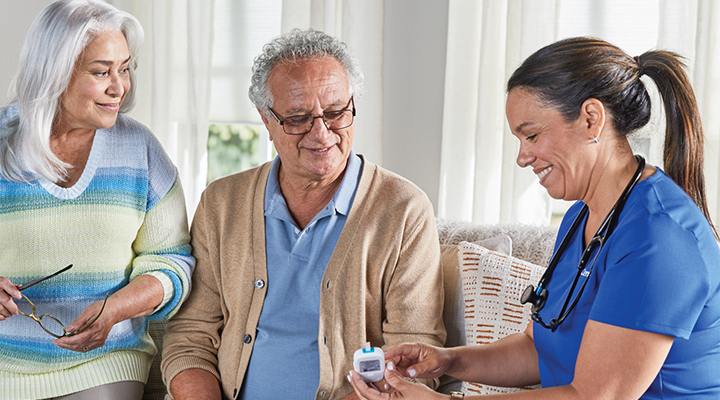 CenterWell Home Health clinician explaining a glucose monitor to a patient and a family member